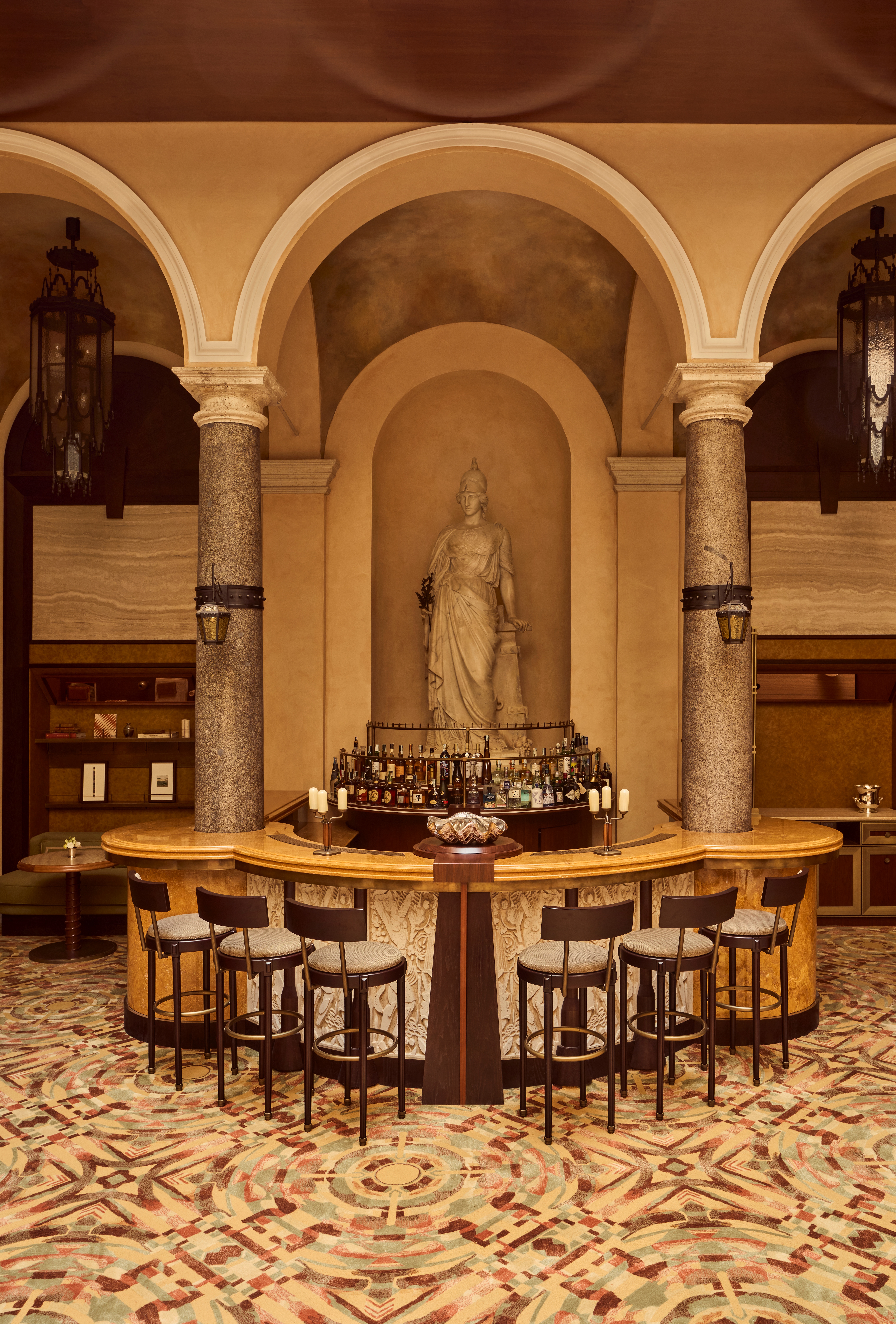 The interiors of a palatial hotel housed inside a 16th-century building with frescoed walls, textural arches, mesmerizing flooring, and plenty of wood oozes antique-inspired furniture and a golden atmosphere across sculptural furnishings, artworks, and plants.