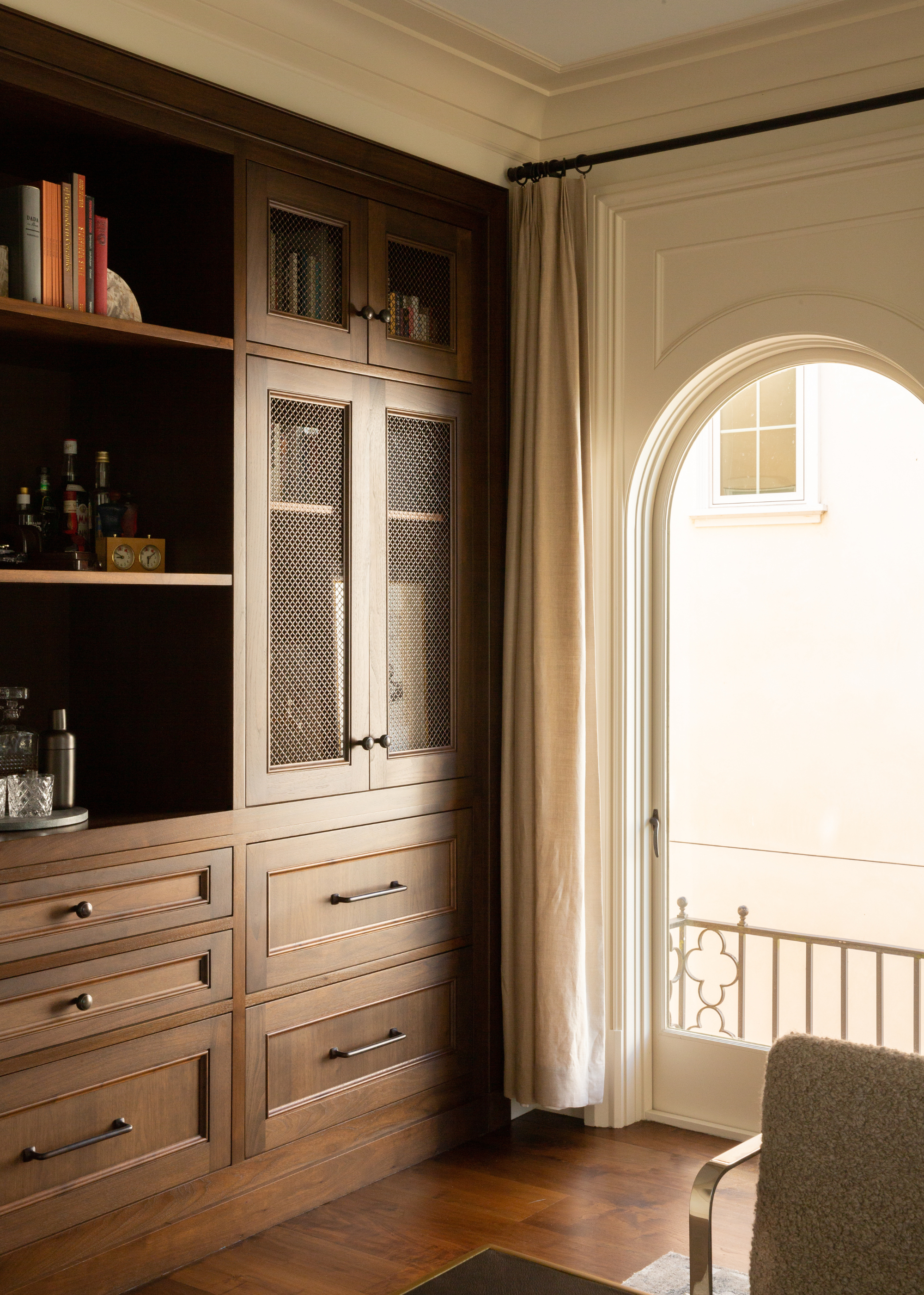 A living room with an arched window, a hosting closet and bar with wooden cabinetry