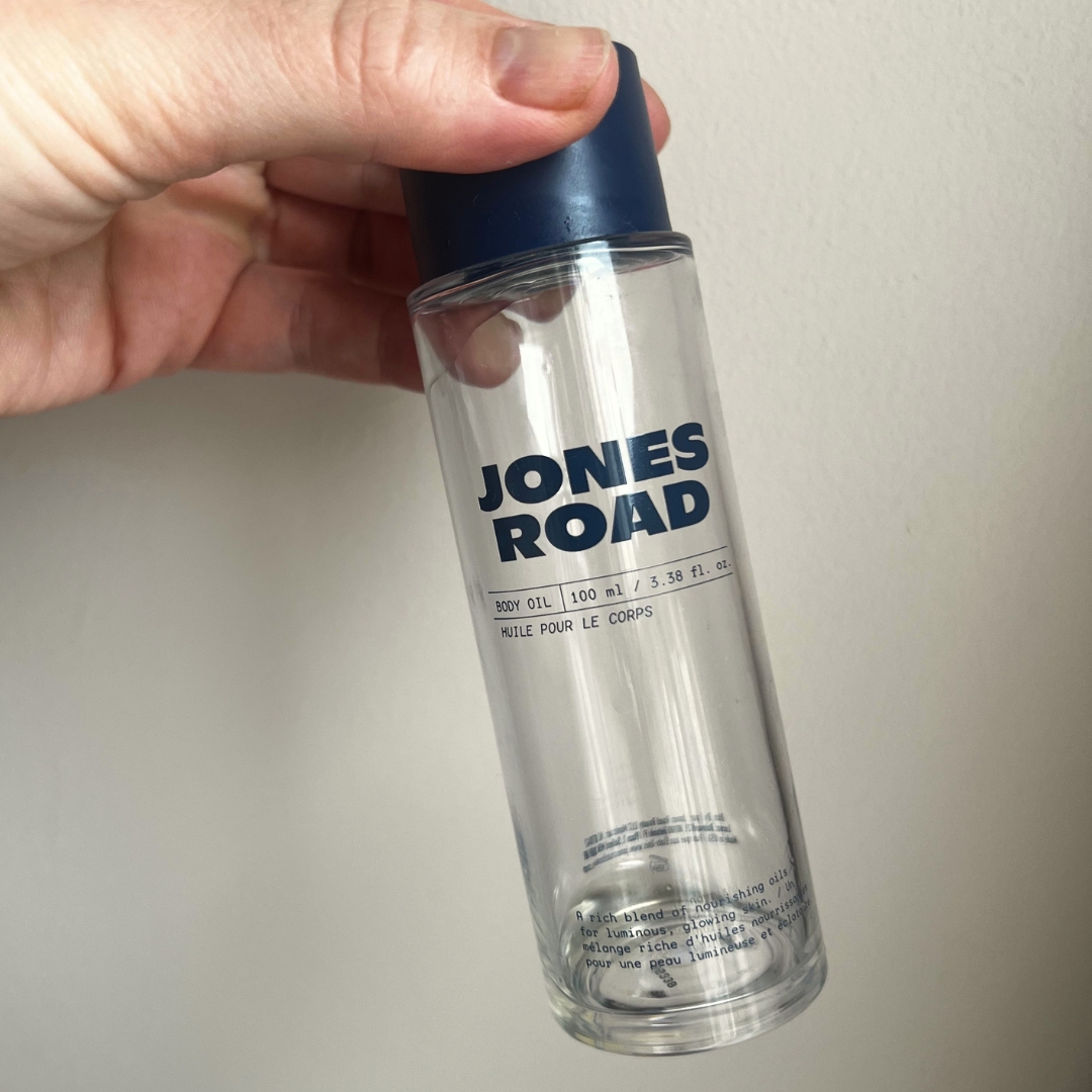 Hand holding empty bottle of Jones Road Body Oil