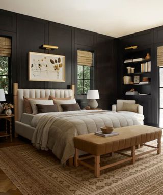 Beige and brown bedding on a bed on a beige carpet against navy walls, hung with wall art and shelves.