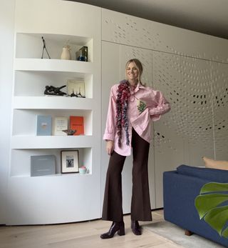 Sue Williamson in a pink button-down shirt and brown pants inside her apartment.