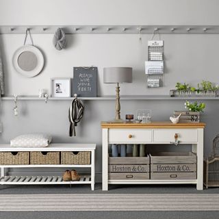 A grey and white hallway with a bench seat, console table and wall pegs