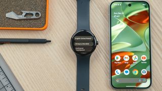 Google Pixel Watch on wood desk next to smartphone showing screen with language selection options