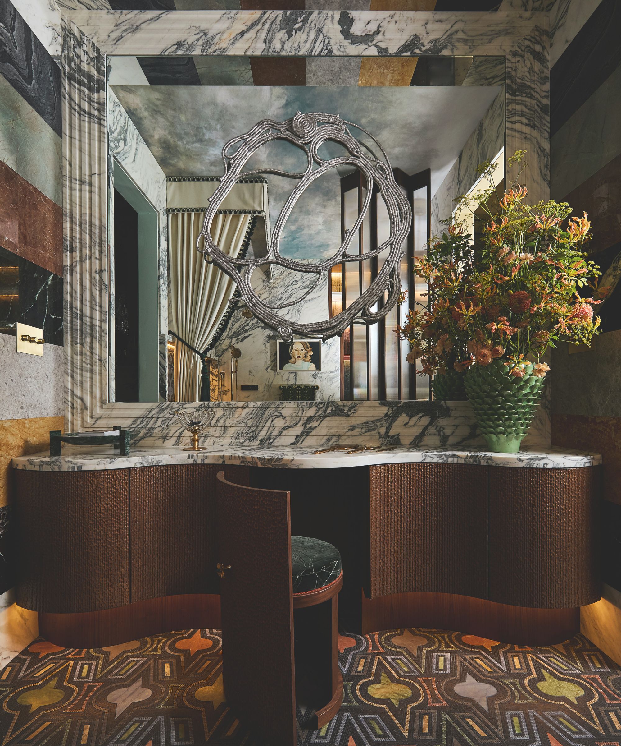 A theatrical bathroom with a large mirror framed by fluted marble, a dark wood vanity, and a patterned carpet