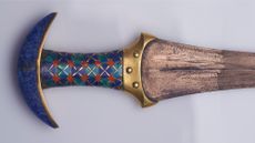 A close up of a blue and brown dagger against a white background