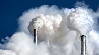 Data center carbon emissions concept art showing white plumes of smoke emitting from chimney stakes at an industrial plant.