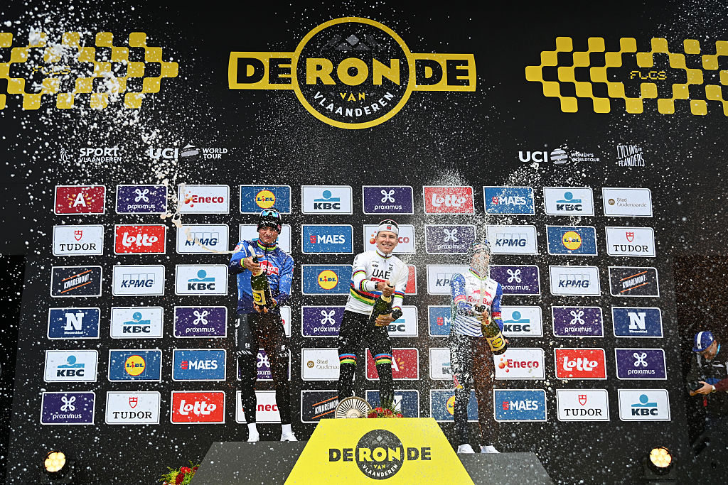 wide view of three riders on the podium all spraying champagne