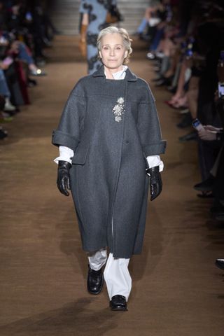 Miu Miu model wearing a grey coat with crystal brooches on the runway