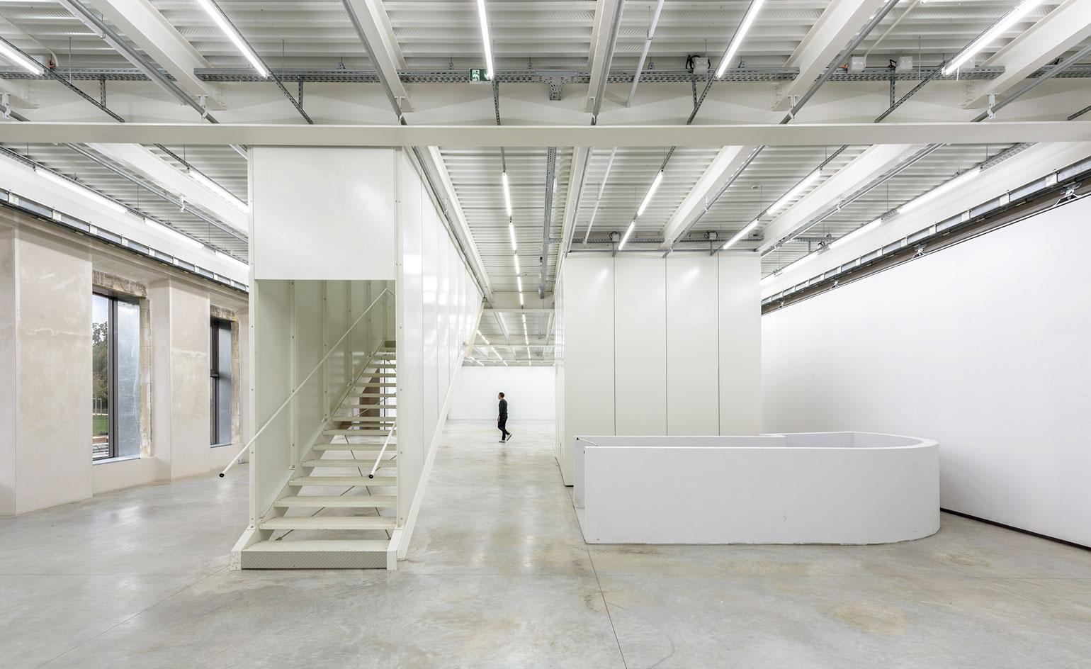 Large open space inside contemporary château with white stair well and light reflective surfaces all around.