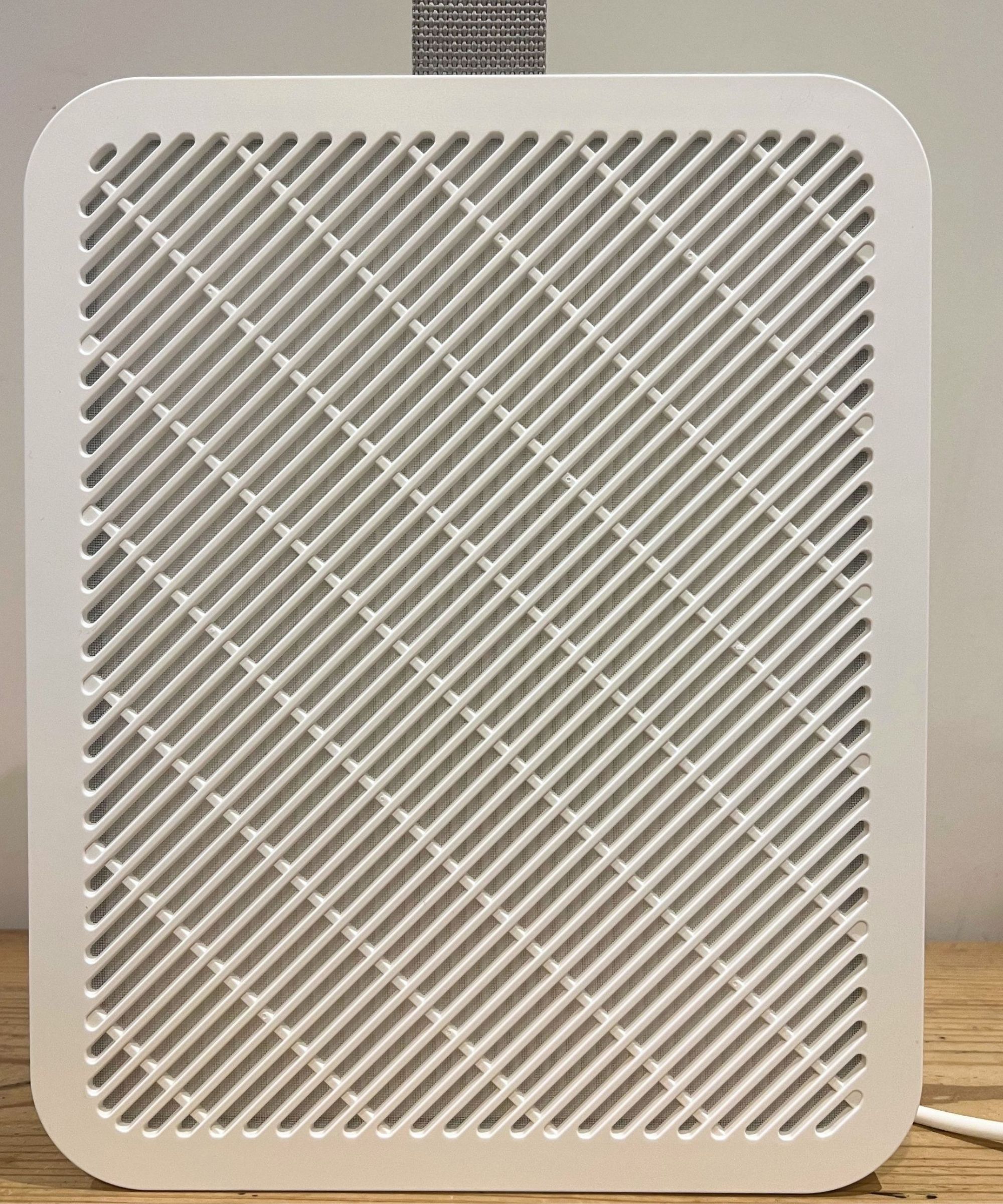 A white IKEA UPP&Aring;TVIND Air purifier with a white cable and grey carry handle on a wooden table against a white wall.