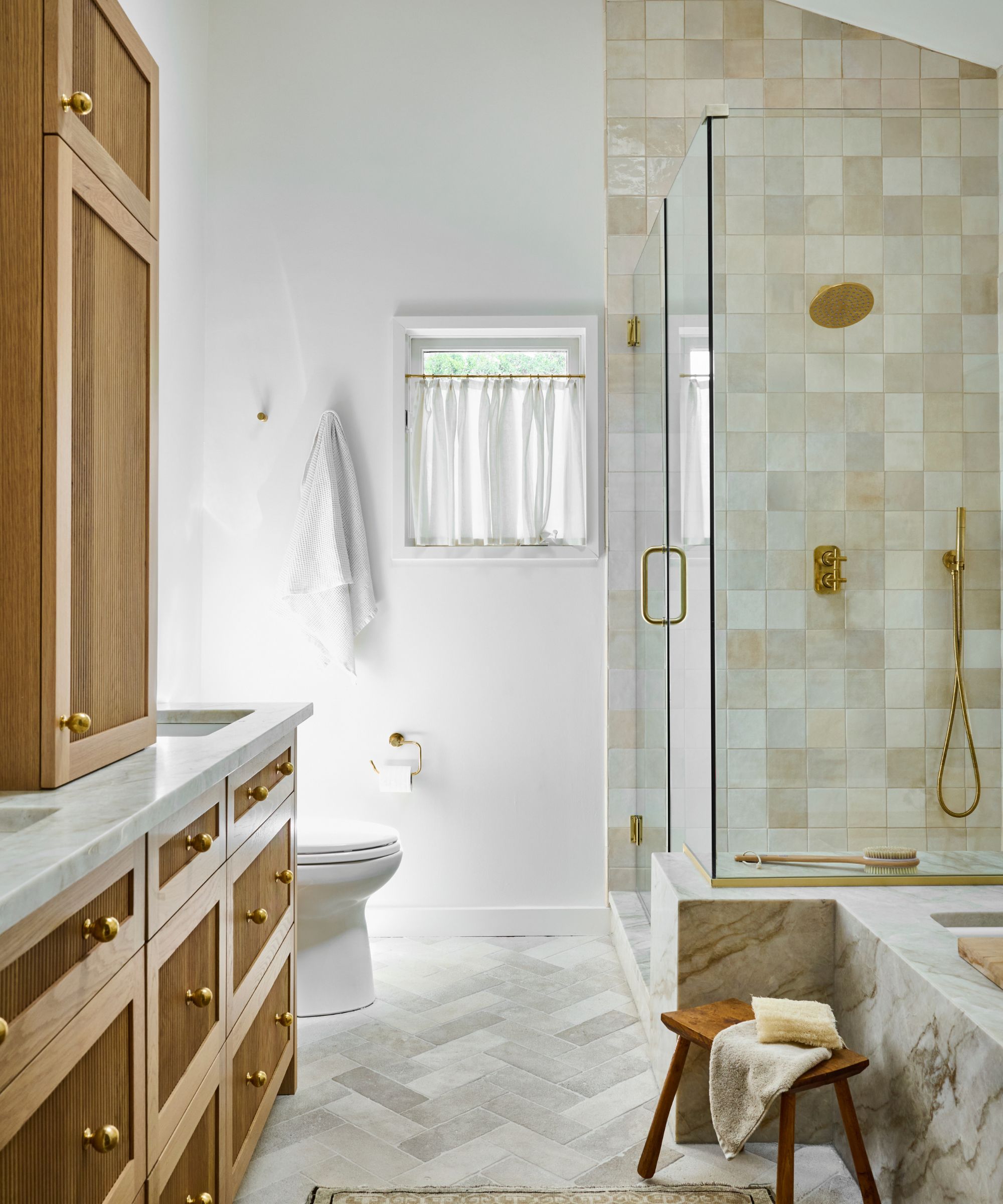 A neutral bathroom with a wooden vanity and cabinetry, and warm-toned tiles throughout