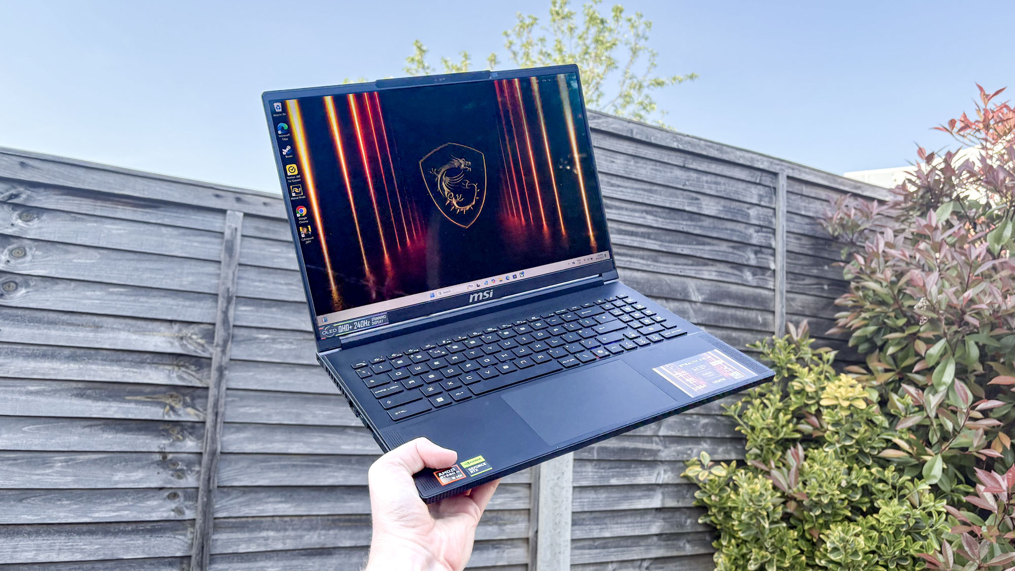 MSI Stealth A16 AI+ open in hand being held up to sky with fence in background
