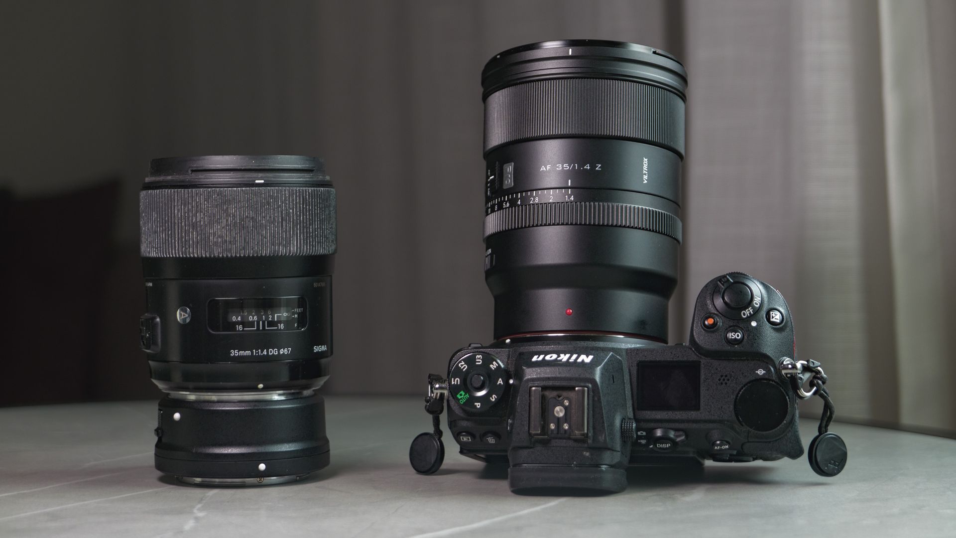Viltrox AF 35mm F1.4 Pro lens attached to a Nikon mirrorless camera, alongside the Sigma 35mm f1/.4 DG Art lens with Nikon F to Z-mount adapter, on a white marble table