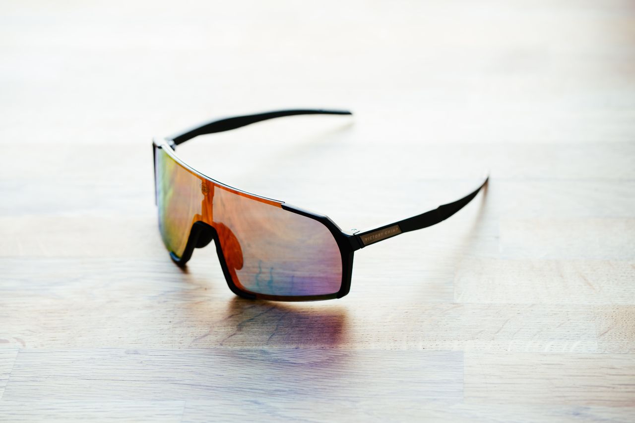A set of black frame sunglasses with irridescent lenses on a wooden surface