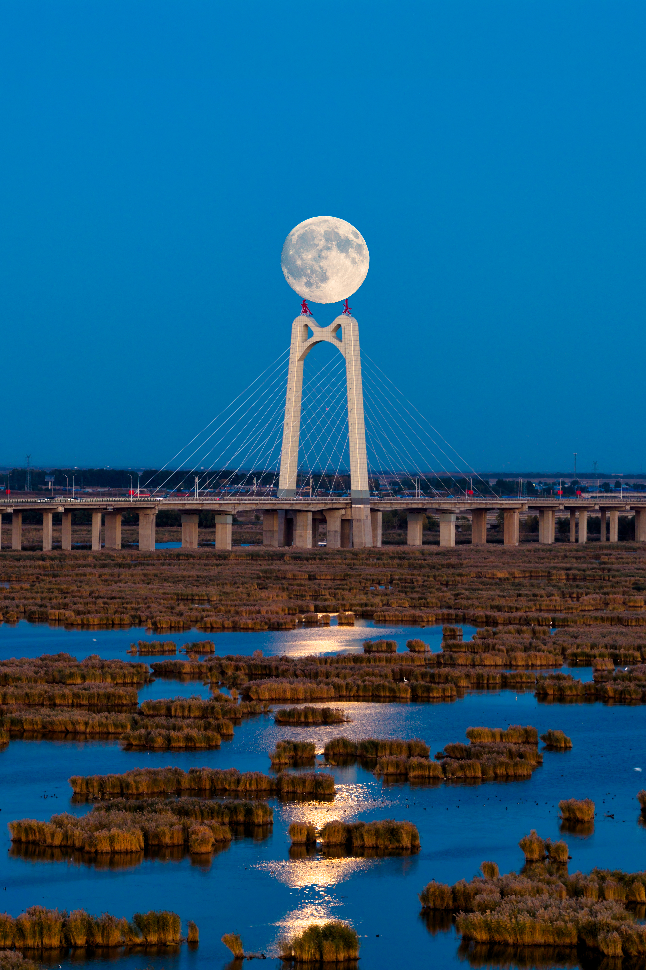 A photograph of the rising Harvest supermoon aligned with the top of a bridge in Daqing, China.