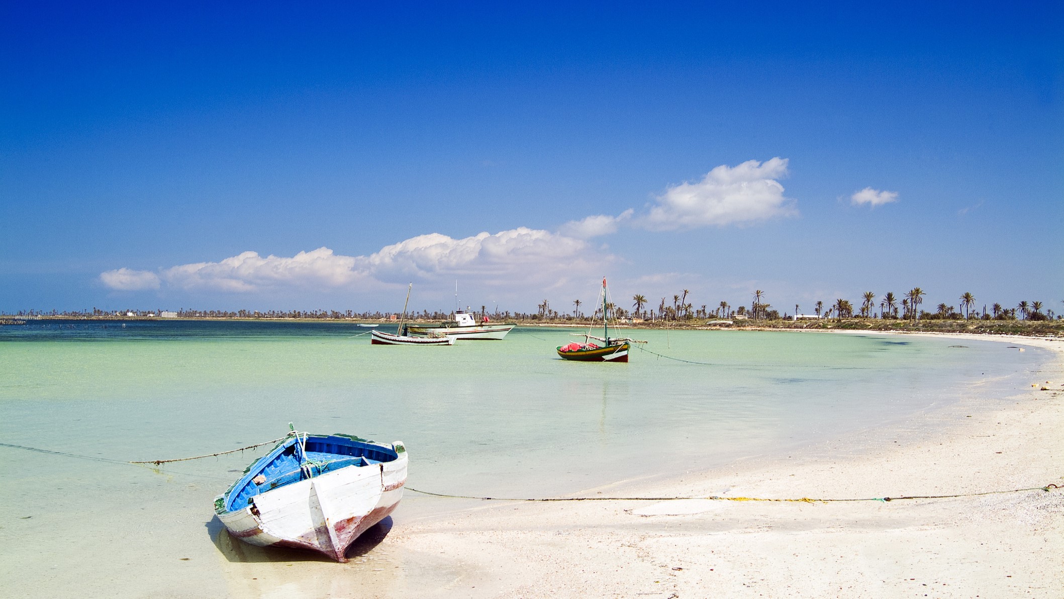 Beach at Chergui island, Kerkennah Islands, Tunisia, North Africa. a small boat is in the foreground moored up to the white sandy beach with blue sky above.