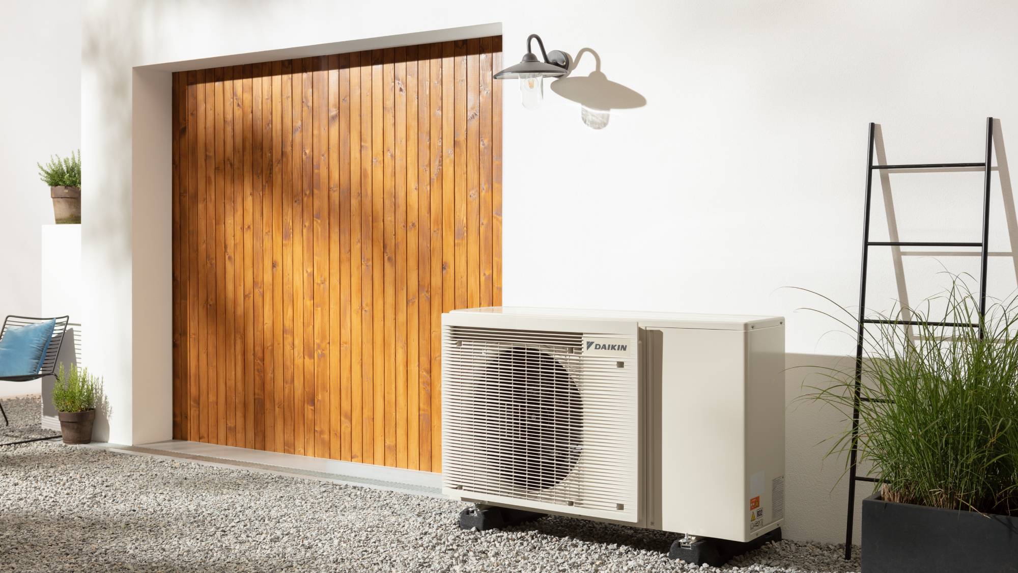 heat pump installed on property with white rendered walls, large wooden doors and gravel patio