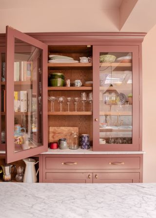 Glass cabinets with double doors. Inside the deep pink cabinets are wine glasses and plates.