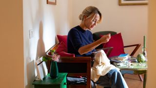 Woman sitting on sofa, darning a cashmere sweater