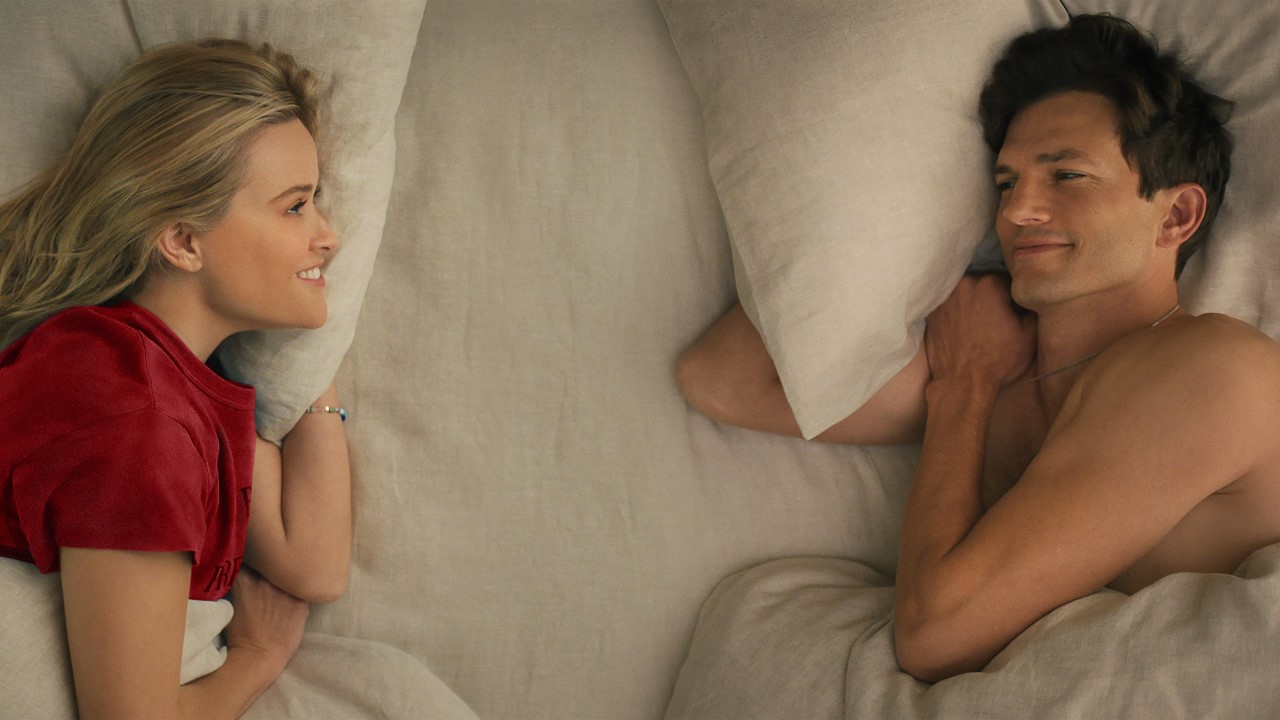 Reese Witherspoon and Ashton Kutcher lie in bed smiling, facing each other but far apart in Your Place or Mine.