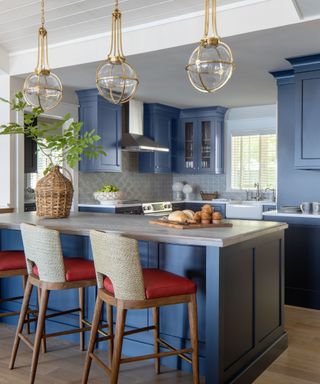 kitchen with blue units and island with upholstered bar stools and three glass pendants