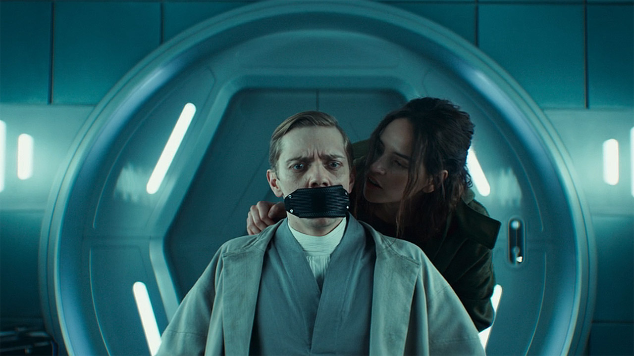 Bix putting a brace over a seated Doctor Gorst's mouth in Andor season 2 episode 6