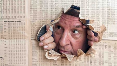 photo of a worried face looking through a hole in newspaper stock listings