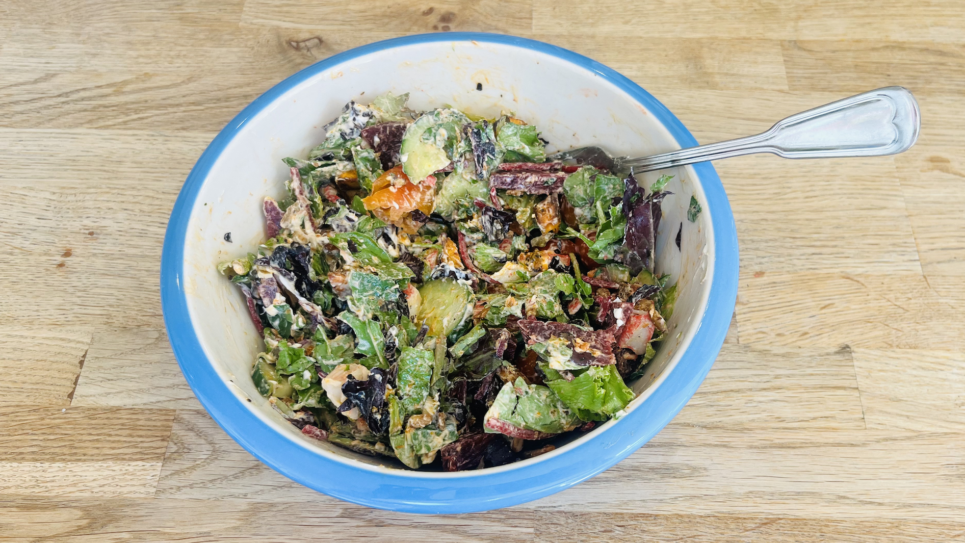 Bowl of salad covered in dressing with fork resting on side of bowl