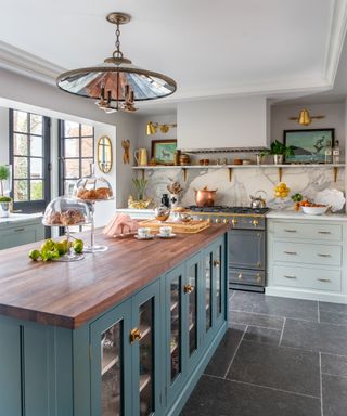 Kitchen lighting ideas with a mirrored lampshade light fixture over a teal island with glass fronted cabinets