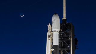 A white and black rocket on the launch pad with the crescent moon in the night sky