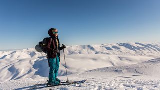A woman on skis and wearing a Patagonia Women’s Storm Shift Jacket stands on a snowy slope.