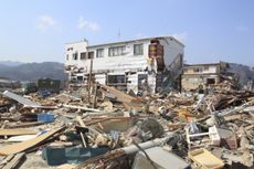 A damaged house standing among rubble after an earthquake.