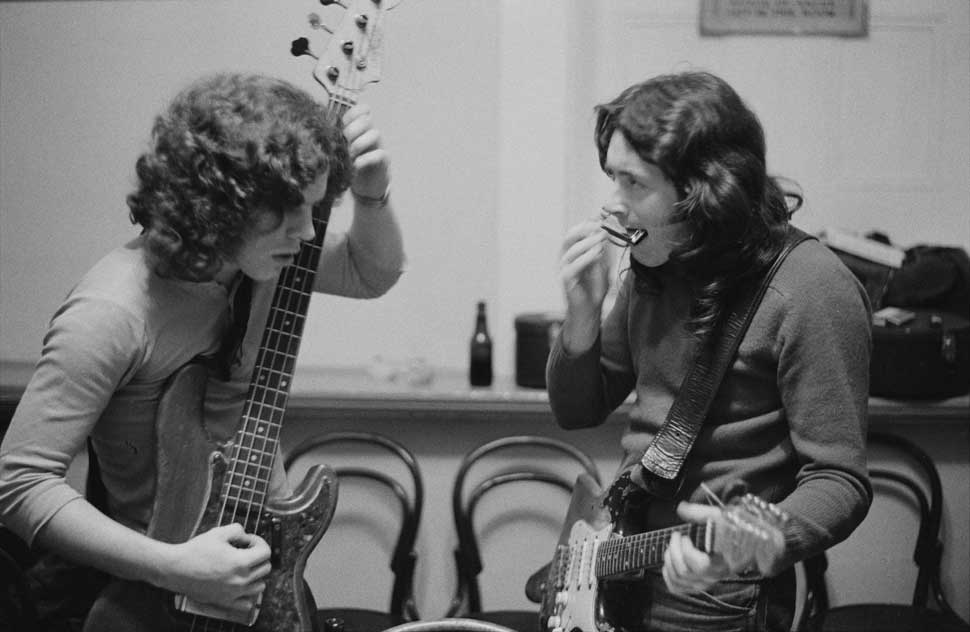Irish singer and guitarist Rory Gallagher (1948-1995) with his Fender Stratocaster strapped on, plays a harmonica backstage with bass guitarist Gerry McAvoy prior to a concert at Leeds City Hall in Leeds, England on 25th March 1972