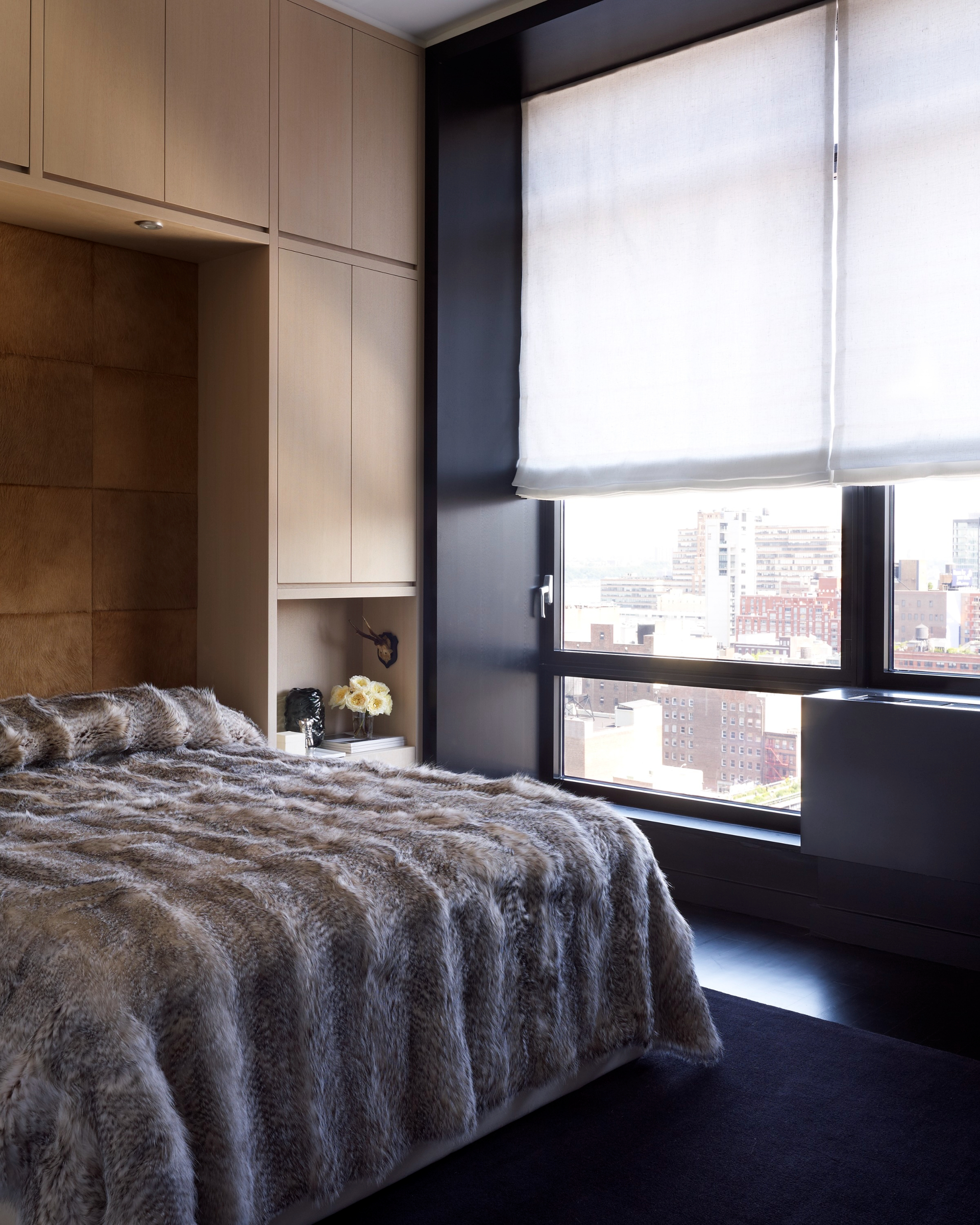 Luxurious contemporary apartment with a fur bedspread and a large window with a city view as well as chic wood panelling