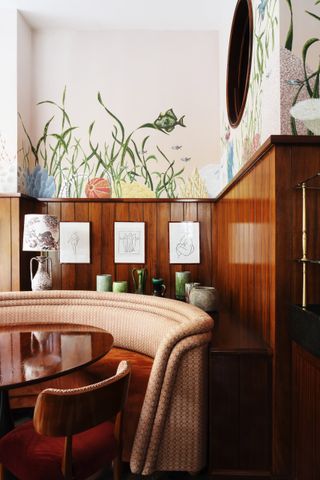 An inventively decorated restaurants features walls painted with nature-inspired motifs, wooden paneled walls, circular stripy banquettes, and ceramics.