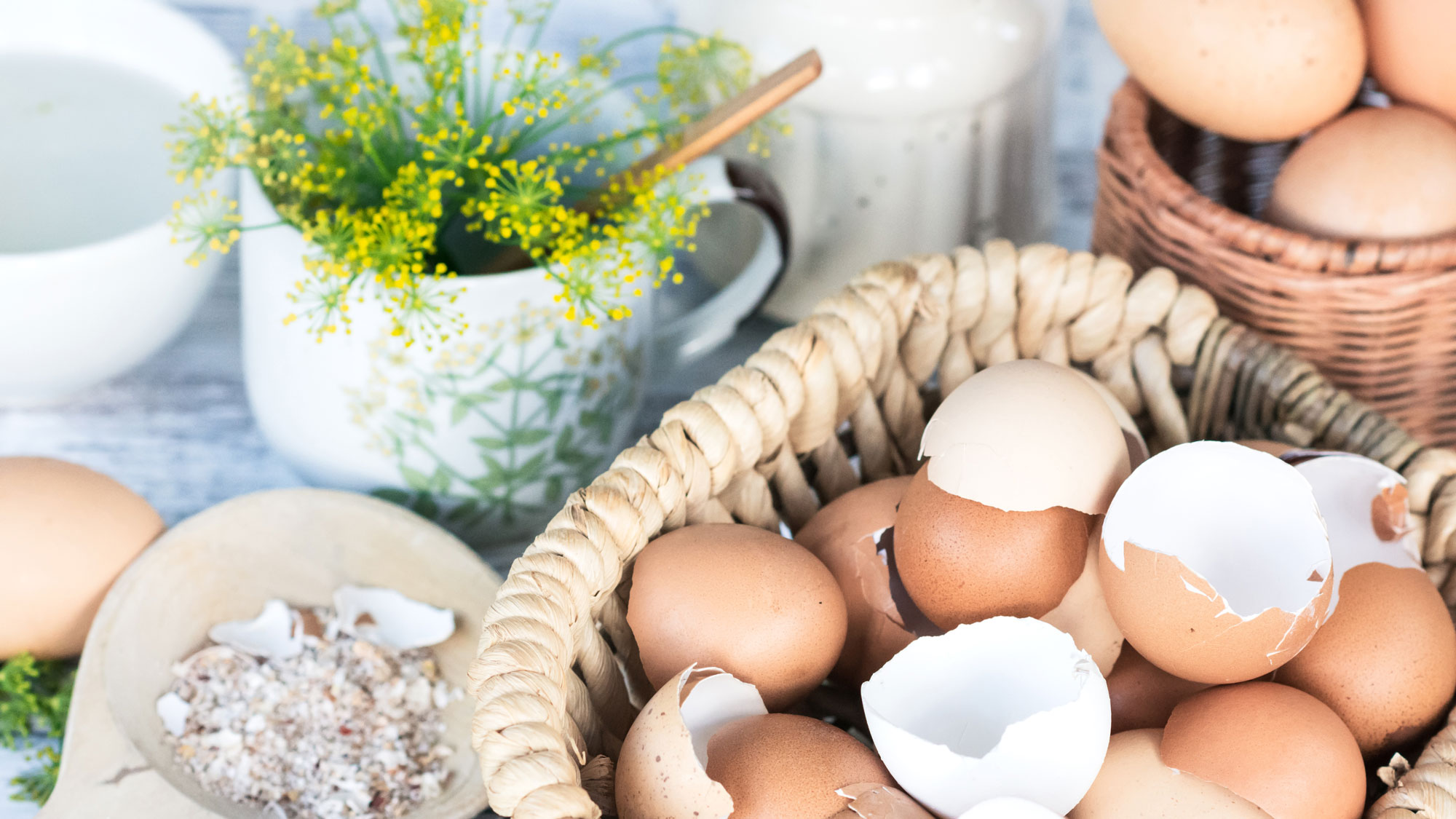 eggshells in wicker basket with wooden spoon and vase of flowers