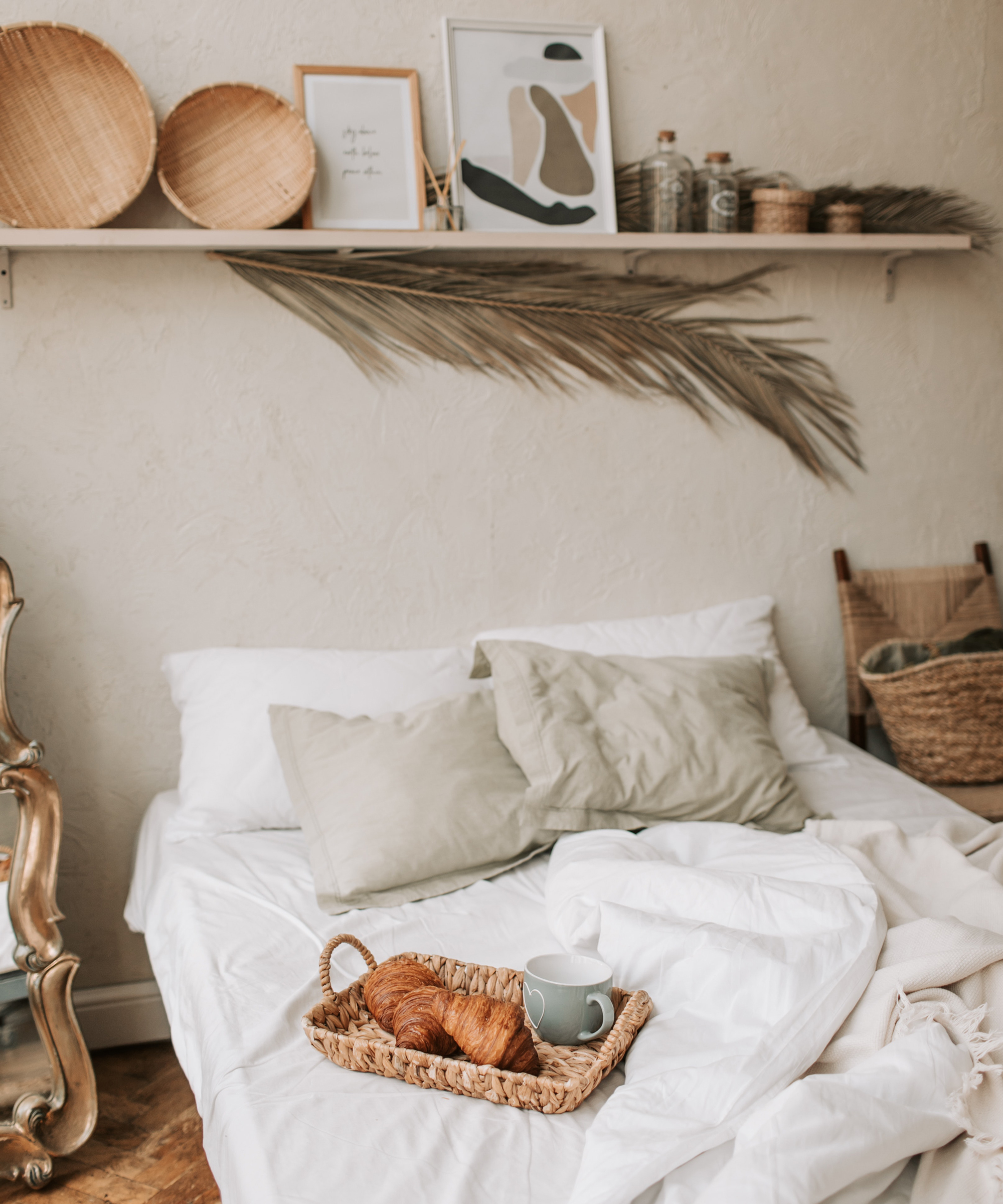 A bedroom with shelf above bed and croissants in woven tray