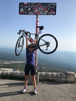 Cyclist Lucy Collins holds a bike over her head at the top of Mount Ventoux