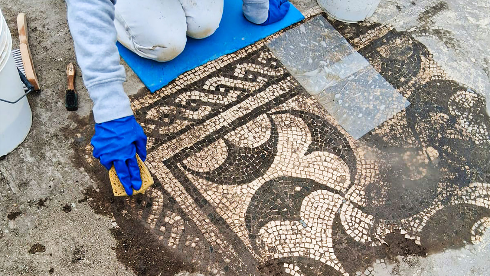 archaeologists work at an ancient Roman site revealing mosaic floors and frescoed walls of a villa