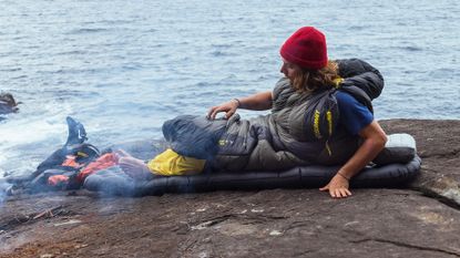 best sleeping bag: man warming his feet by the campfire while in a sleeping bag