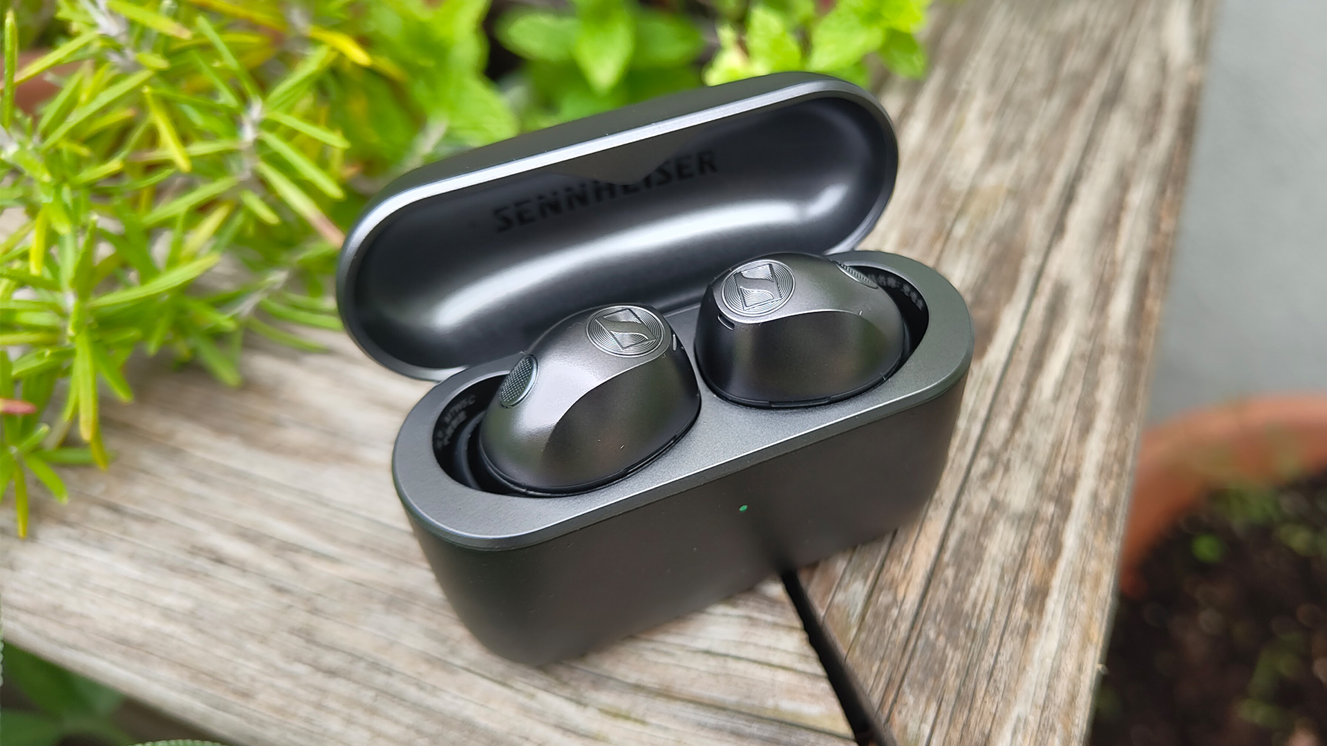 Sennheiser Momentum True Wireless 5 wireless earbuds in case on corner of wooden planter