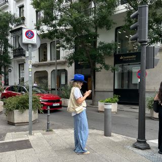 Woman wearing baggy white t-shirt, baggy striped pants, off-white bag, and bright blue cowboy hat.