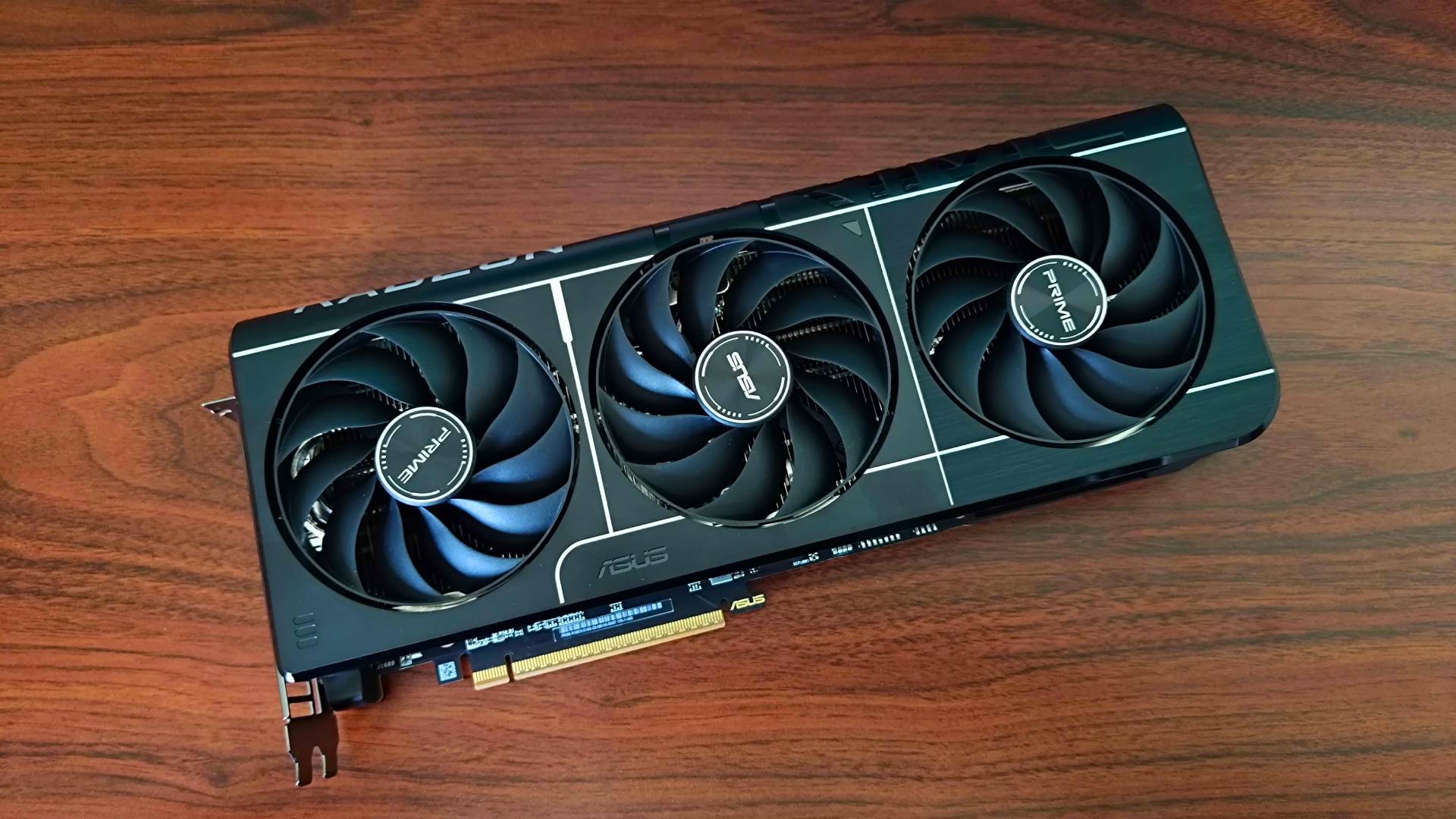 AMD Radeon RX 9070 Asus Prime graphics card lying flat on woodgrain desk with fans facing upwards.