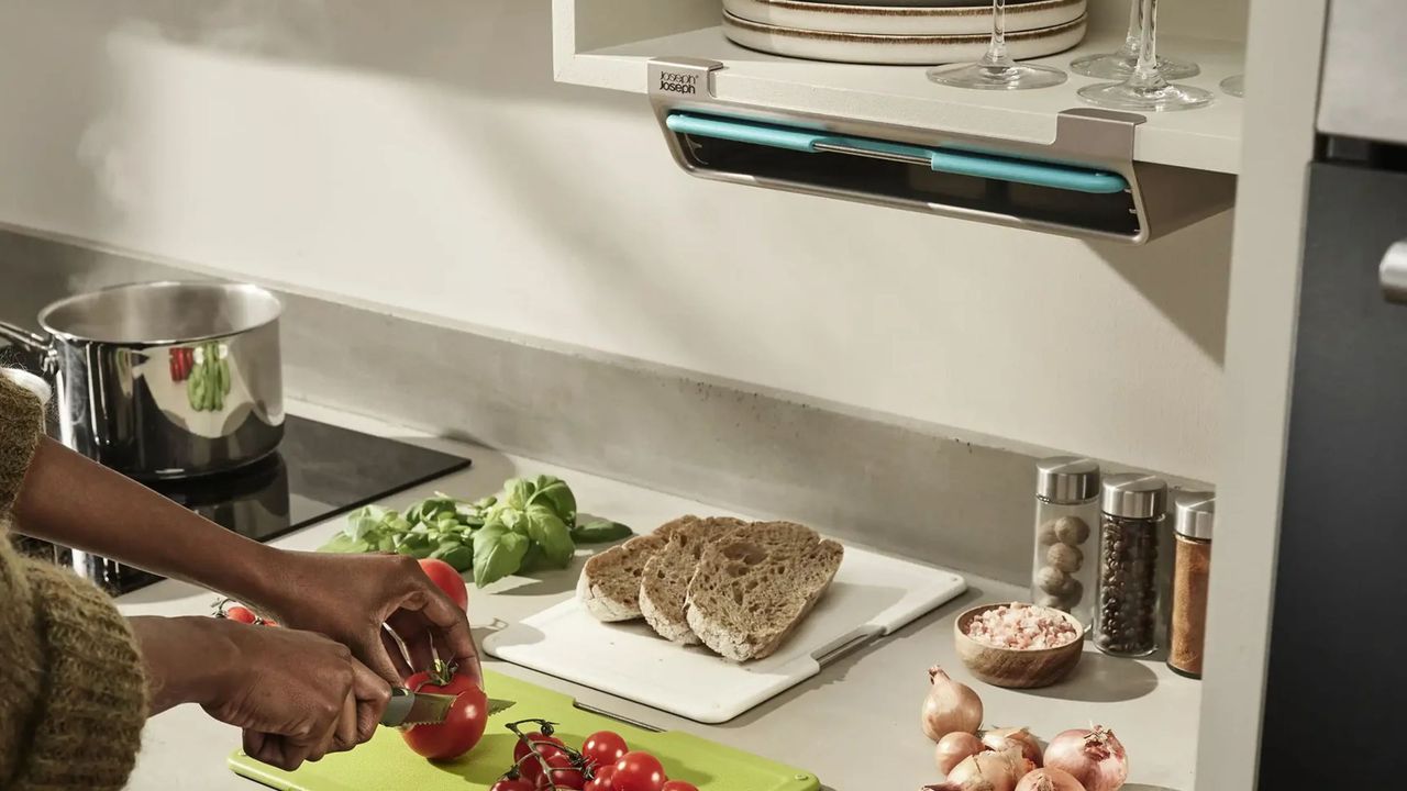 kitchen counter with person chopping up tomatoes and bread on cutting boards next to the stove with a under-shelf mounted holder