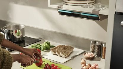 kitchen counter with person chopping up tomatoes and bread on cutting boards next to the stove with a under-shelf mounted holder