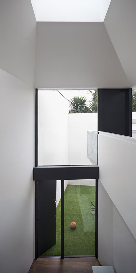 An opened black door in a residential home, leading to a courtyard/play area with green grass. Basket ball and 2 rackets on the grass.