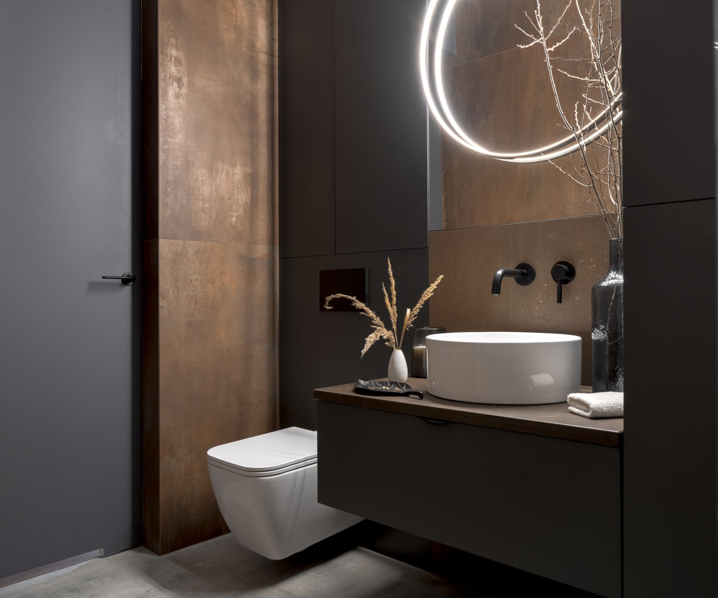 A bathroom with dark brown walls and a lit up mirror