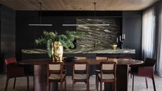 moody dining room with timber ceiling, round large table with leather chairs at either end and rattan chairs along the side, gold vase filled with branches, and a marble bar running along the wall behind