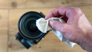 A hand using a cloth to clean a camera lens