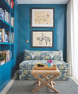 Fitted bookshelves with cupboards below, wooden flooring and rug, blue patterned sofa and drawings of horses on a blue wall.